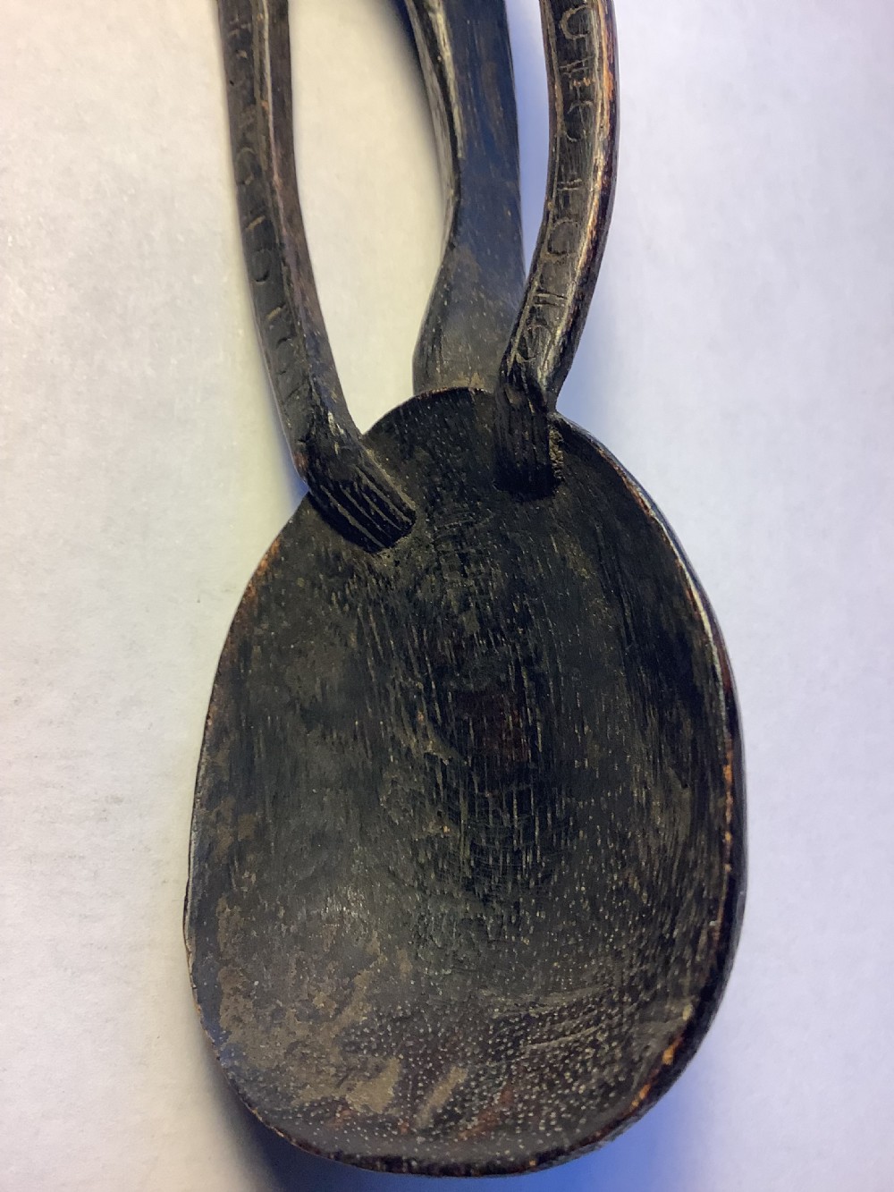 A dark carved wooden spoon featuring a handle sculpted into a stylized human figure with incised geometric markings along the arms. View VI