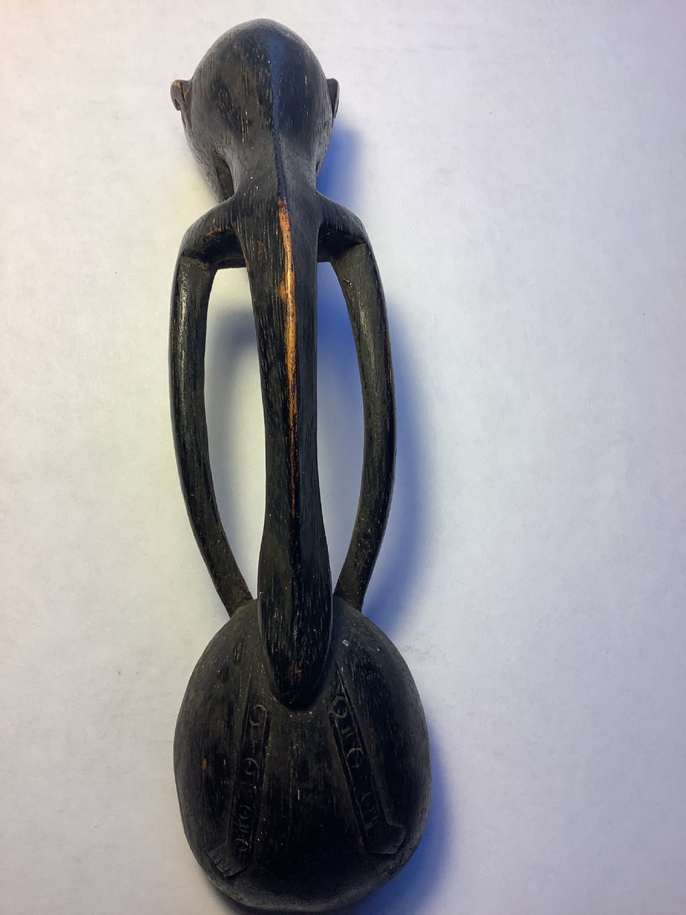 A dark carved wooden spoon featuring a handle sculpted into a stylized human figure with incised geometric markings along the arms. View IX