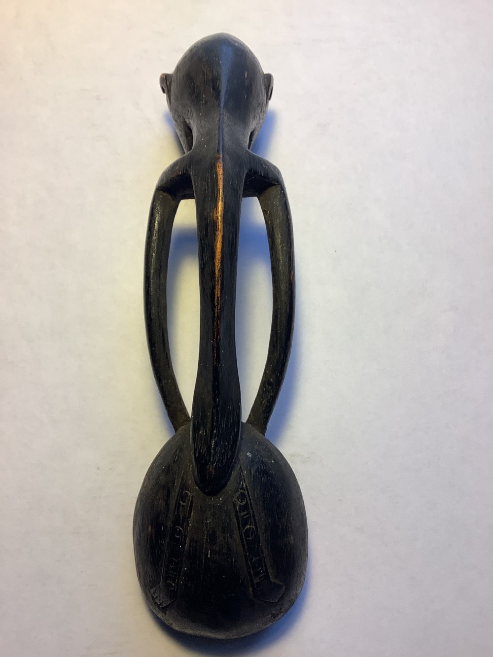 A dark carved wooden spoon featuring a handle sculpted into a stylized human figure with incised geometric markings along the arms. View X