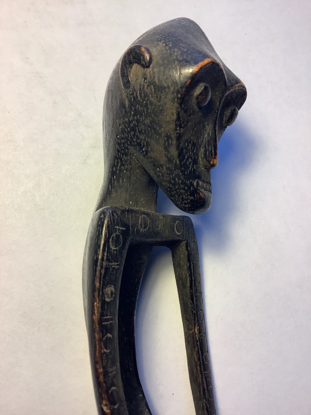 A dark carved wooden spoon featuring a handle sculpted into a stylized human figure with incised geometric markings along the arms. View XII
