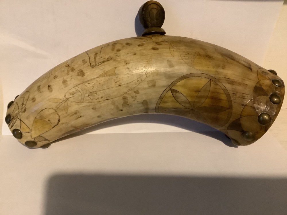 A curved antique powder horn featuring geometric scrimshaw engravings, brass studs along the borders, and a turned wooden plug. View II