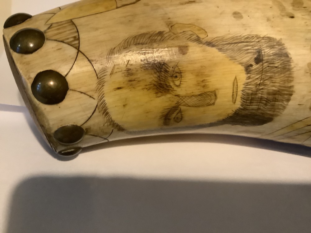 A curved antique powder horn featuring geometric scrimshaw engravings, brass studs along the borders, and a turned wooden plug. View IV