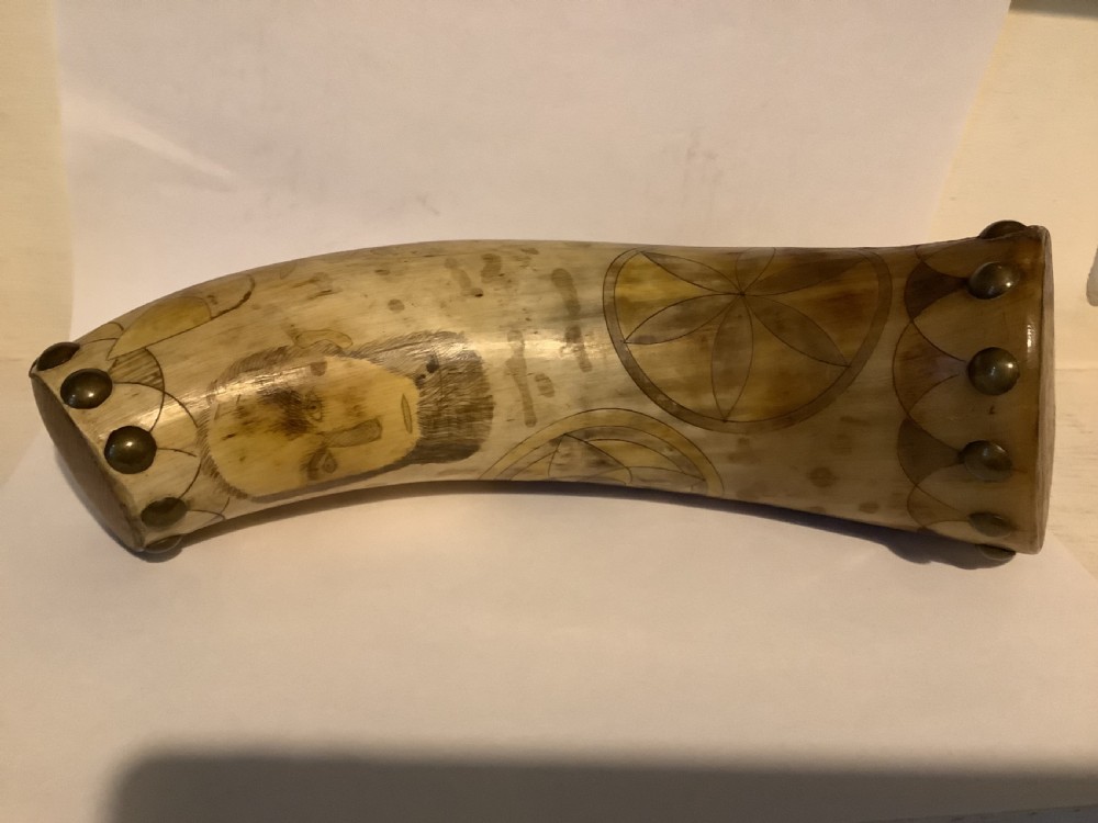 A curved antique powder horn featuring geometric scrimshaw engravings, brass studs along the borders, and a turned wooden plug. View X