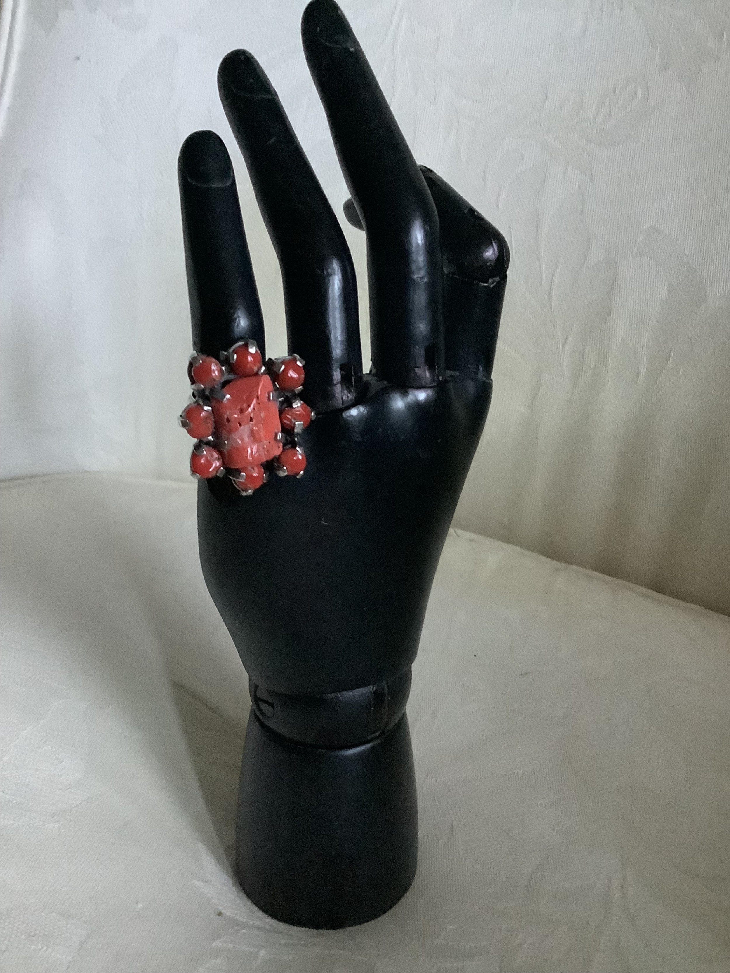 A silver statement cluster ring featuring a rectangular natural red coral centerpiece surrounded by small rounded coral cabochons on a black mannequin display hand.