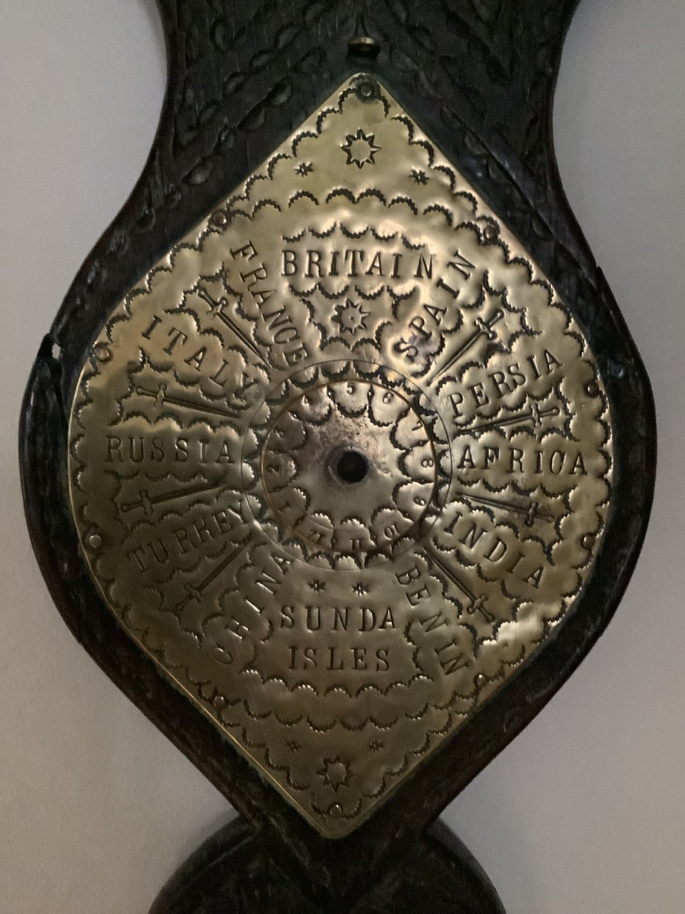 An antique brass sundial and world clock plaque mounted on a carved dark wooden backboard, featuring engraved Roman numerals and global place names. View II