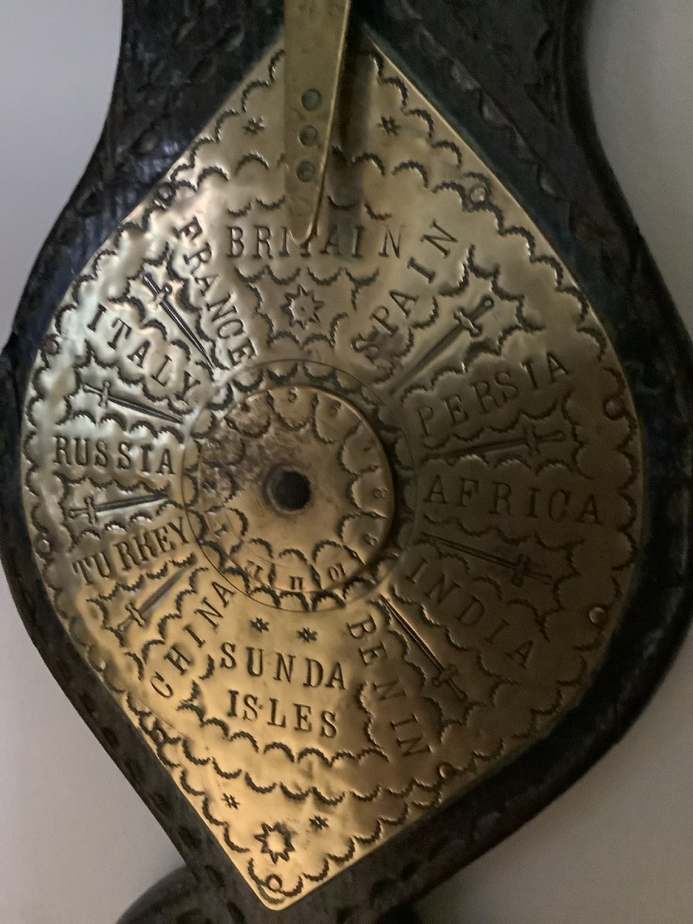 An antique brass sundial and world clock plaque mounted on a carved dark wooden backboard, featuring engraved Roman numerals and global place names. View VII