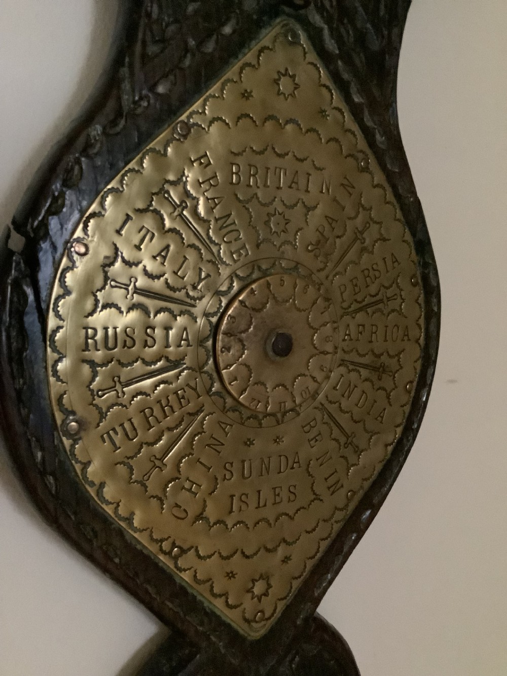 An antique brass sundial and world clock plaque mounted on a carved dark wooden backboard, featuring engraved Roman numerals and global place names. View VIII