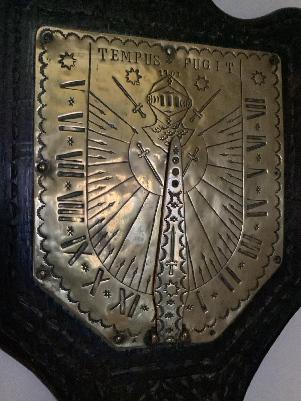 An antique brass sundial and world clock plaque mounted on a carved dark wooden backboard, featuring engraved Roman numerals and global place names. View XIII
