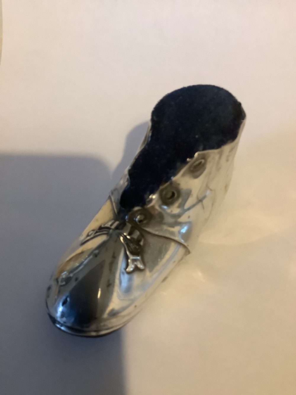 An antique silver pin cushion shaped like a laced boot with a dark velvet top insert.