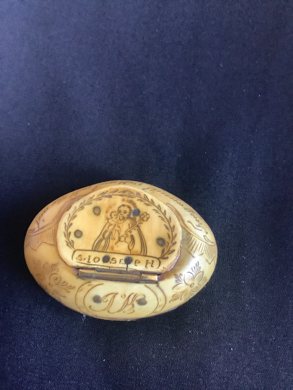 An oval antique horn pocket snuff box featuring hand-engraved depictions of Saint Joseph, floral motifs, and a central brass hinge. View III