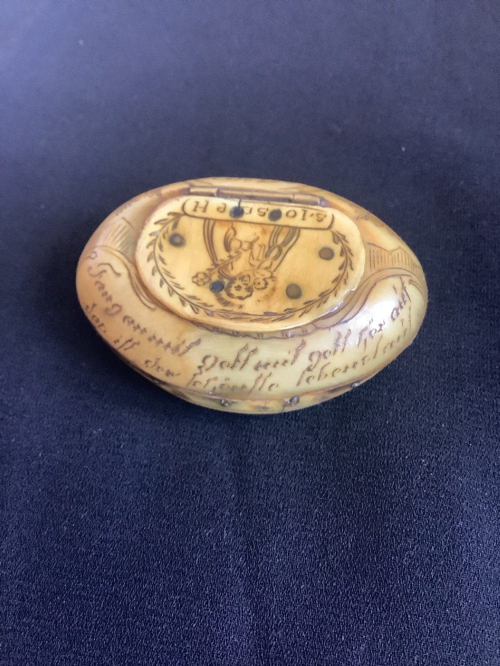 An oval antique horn pocket snuff box featuring hand-engraved depictions of Saint Joseph, floral motifs, and a central brass hinge. View II