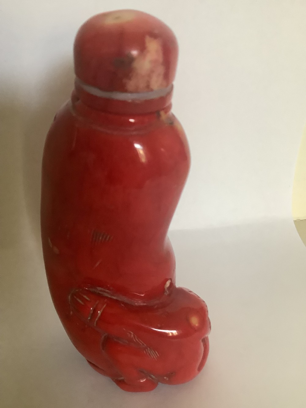 A carved bright red coral Chinese snuff bottle featuring an integrated carved figure at the base and a matching stopper. View V