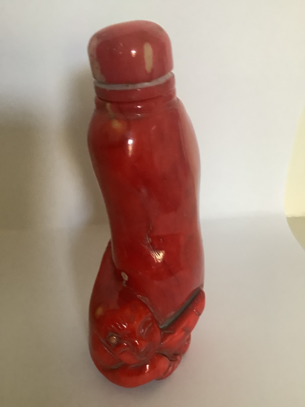 A carved bright red coral Chinese snuff bottle featuring an integrated carved figure at the base and a matching stopper. View II