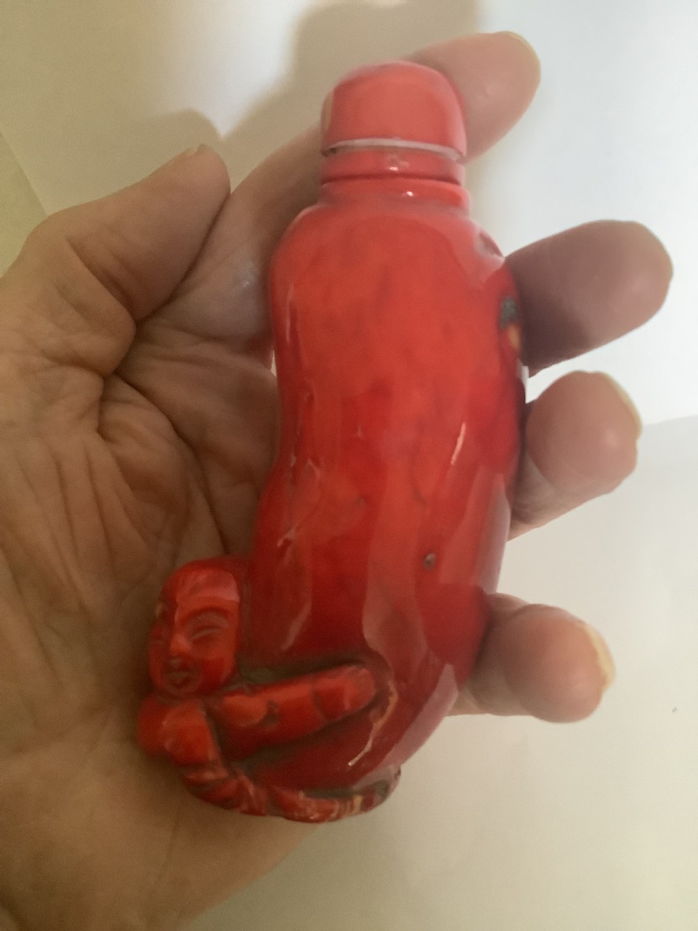 A carved bright red coral Chinese snuff bottle featuring an integrated carved figure at the base and a matching stopper.