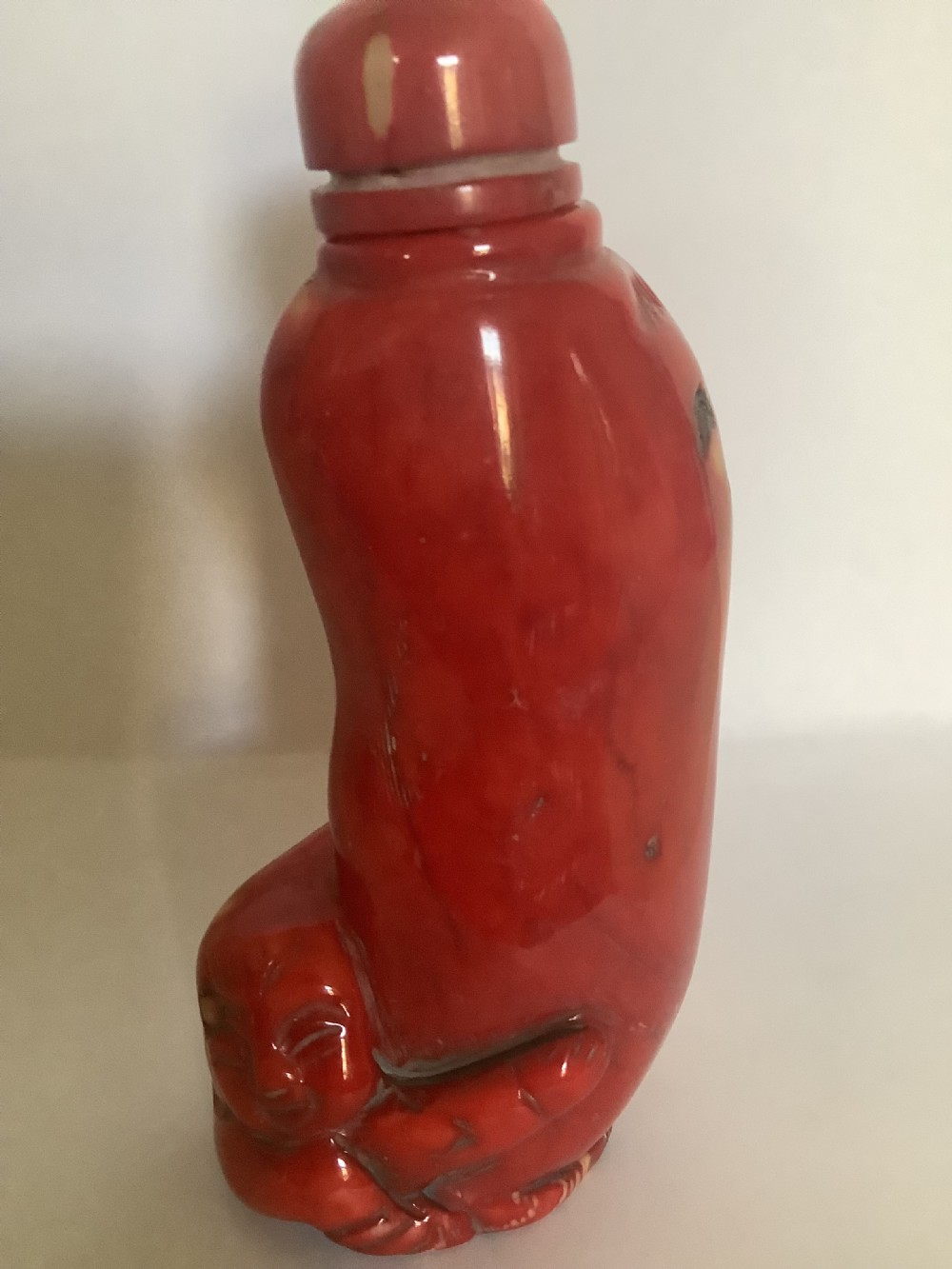 A carved bright red coral Chinese snuff bottle featuring an integrated carved figure at the base and a matching stopper. View IV