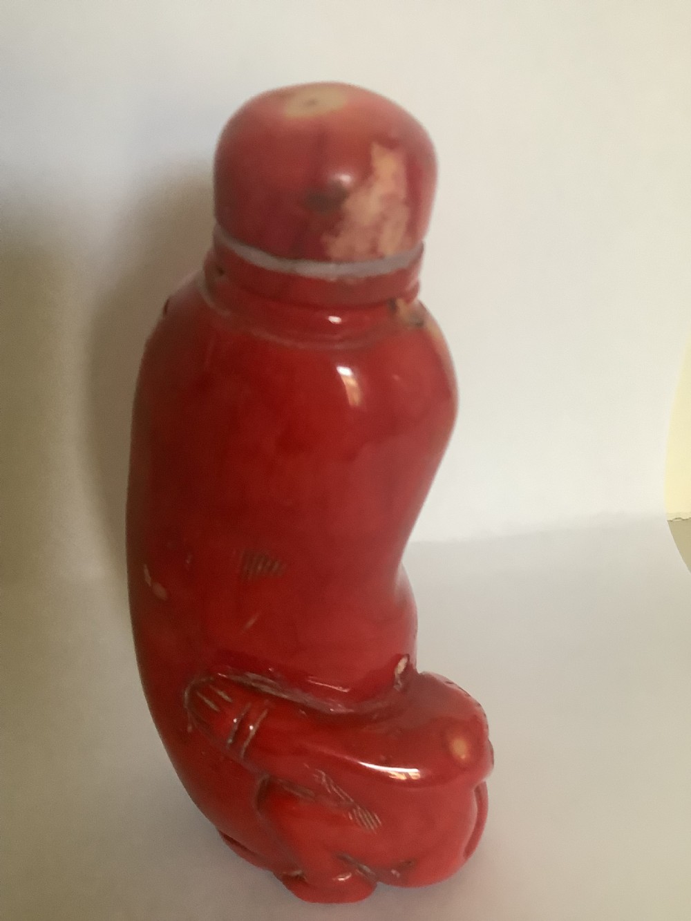 A carved bright red coral Chinese snuff bottle featuring an integrated carved figure at the base and a matching stopper. View VI