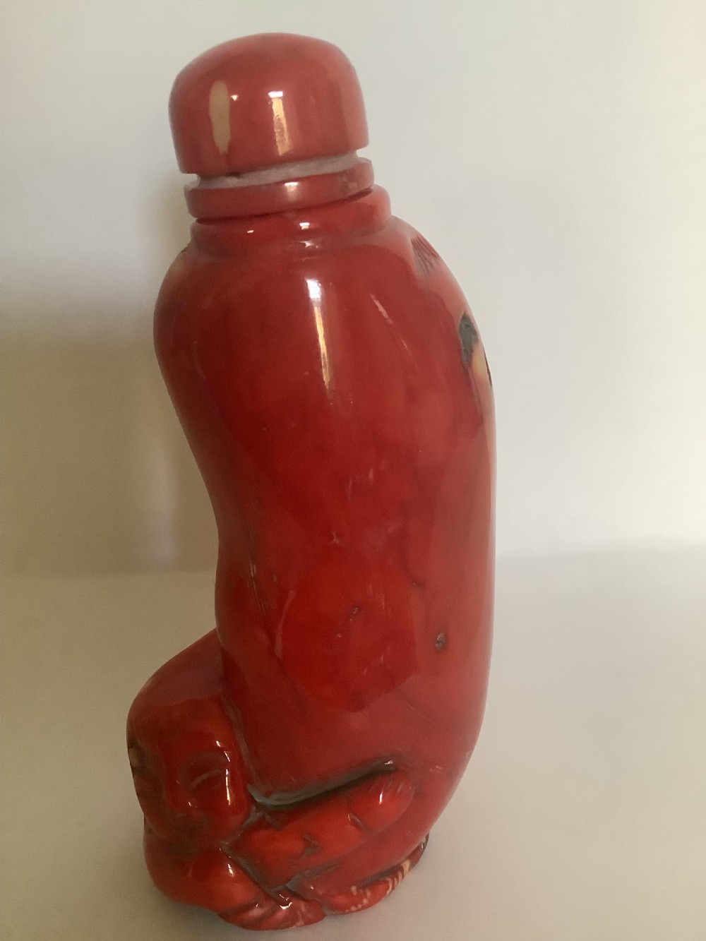 A carved bright red coral Chinese snuff bottle featuring an integrated carved figure at the base and a matching stopper. View VII
