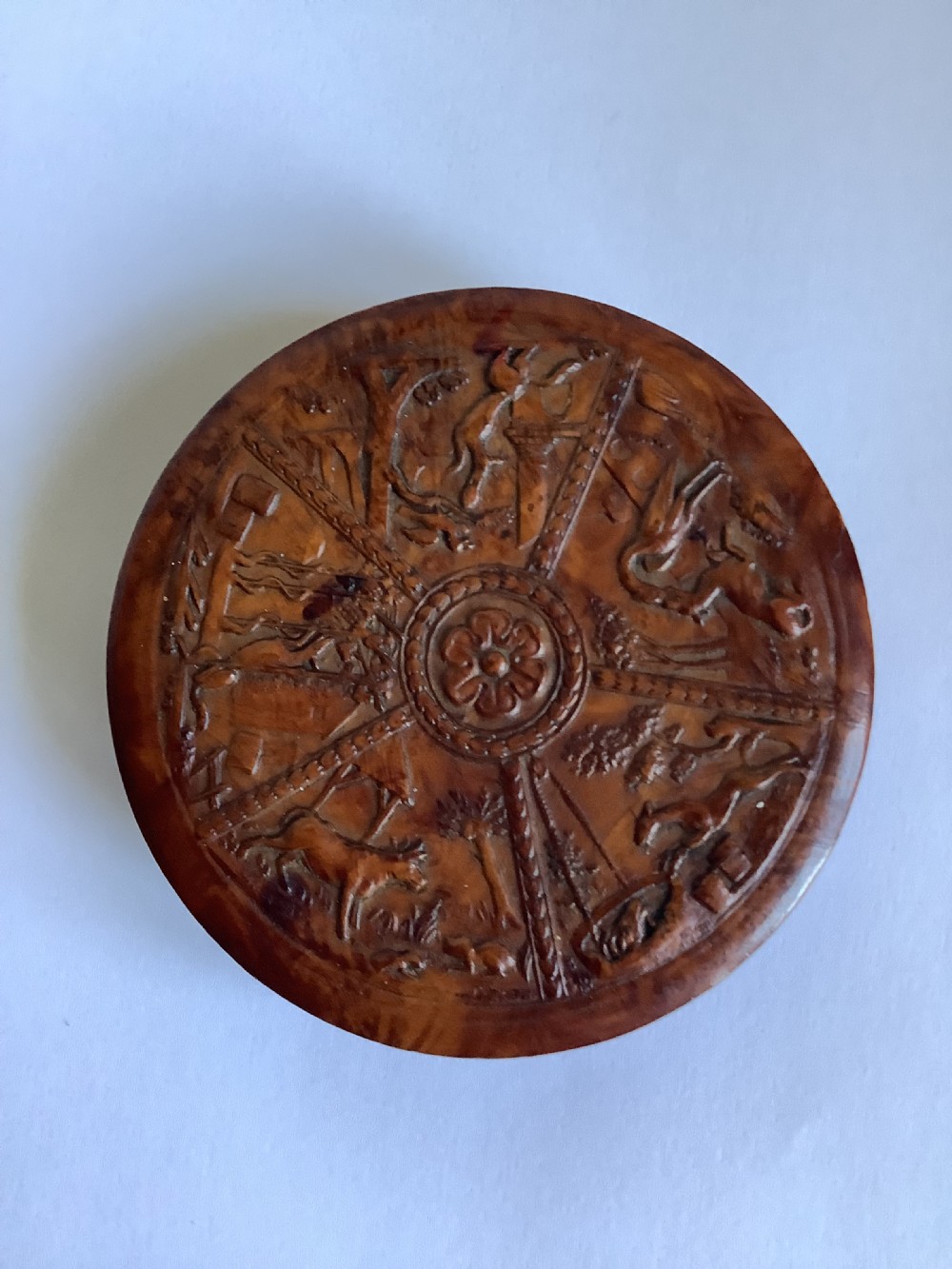 A circular carved burr walnut snuff box featuring segmented radial panels with relief figures and a central floral rosette.
