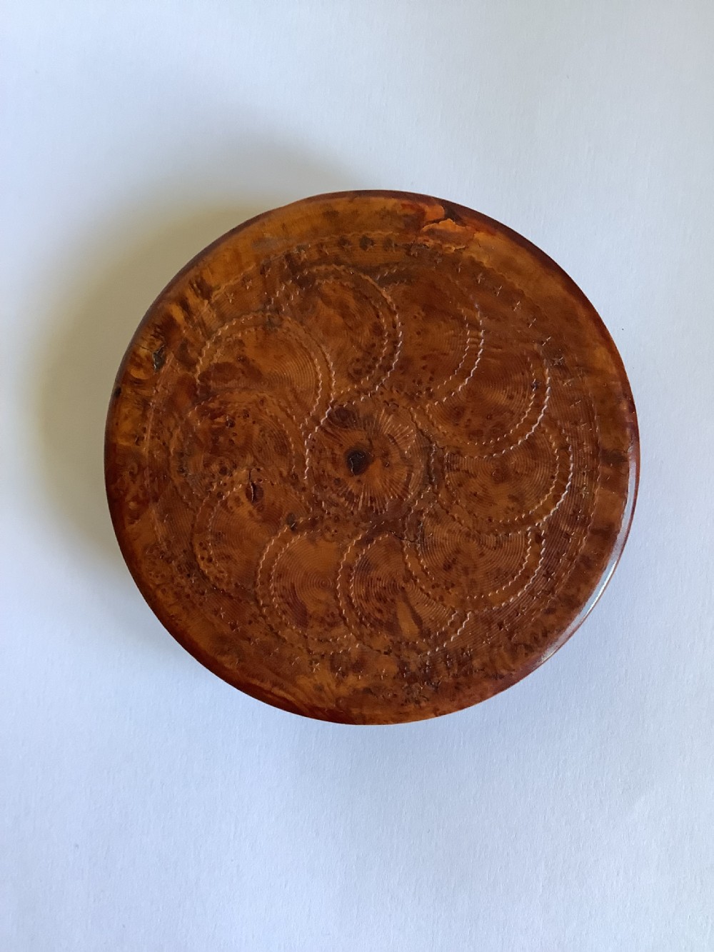 A circular carved burr walnut snuff box featuring segmented radial panels with relief figures and a central floral rosette. View V