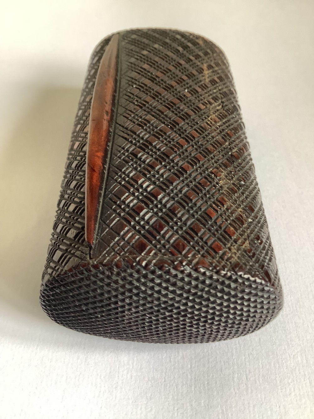 A small hand-carved dark hardwood snuff box featuring a detailed geometric lattice pattern held in a persons hand. View IV