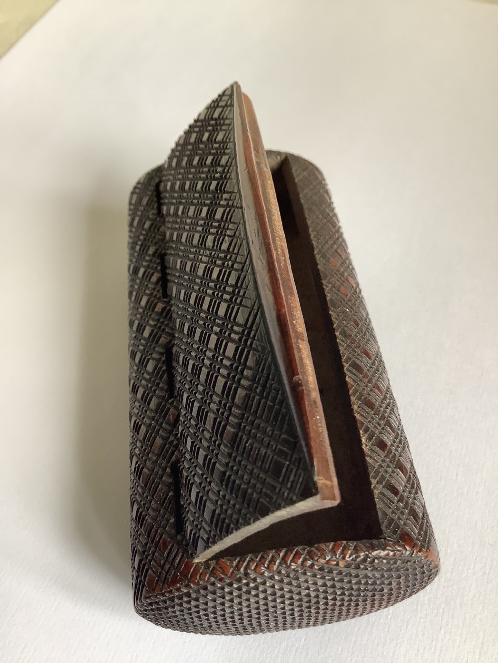 A small hand-carved dark hardwood snuff box featuring a detailed geometric lattice pattern held in a persons hand. View II