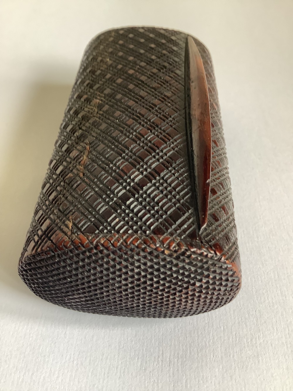 A small hand-carved dark hardwood snuff box featuring a detailed geometric lattice pattern held in a persons hand. View III