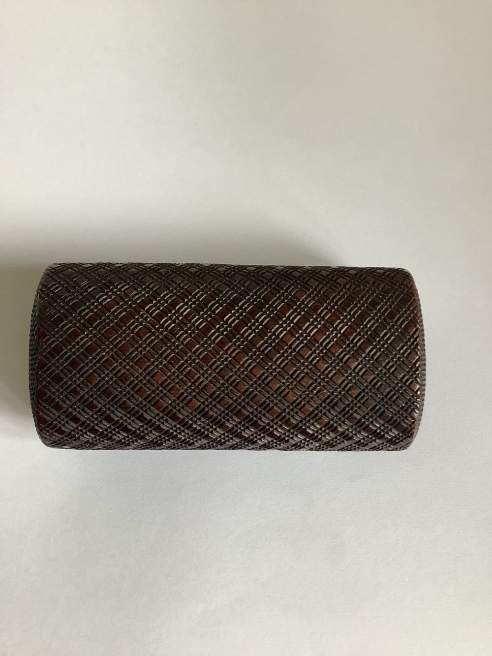 A small hand-carved dark hardwood snuff box featuring a detailed geometric lattice pattern held in a persons hand. View V