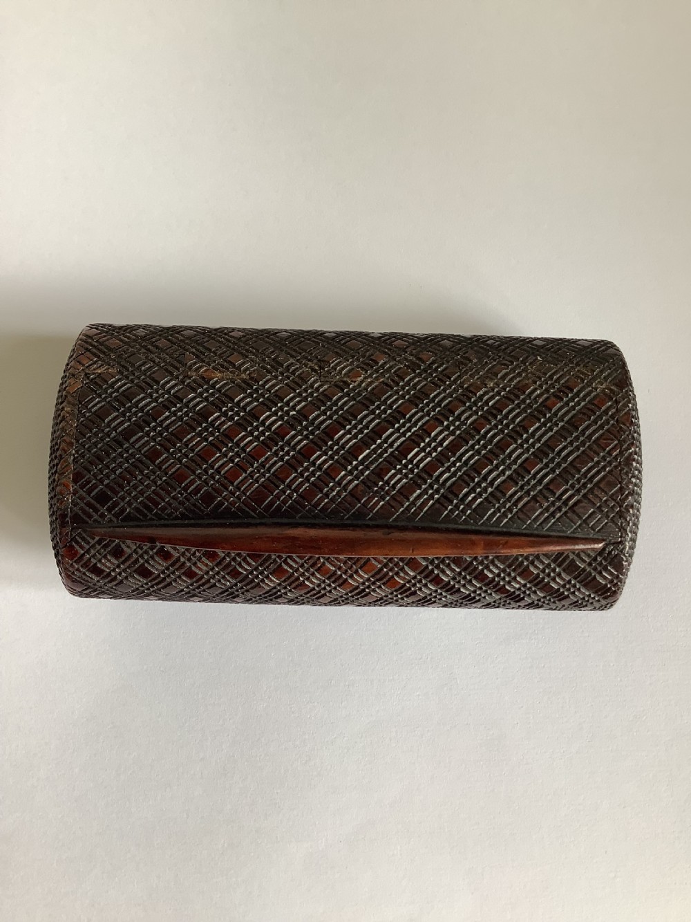 A small hand-carved dark hardwood snuff box featuring a detailed geometric lattice pattern held in a persons hand. View VI