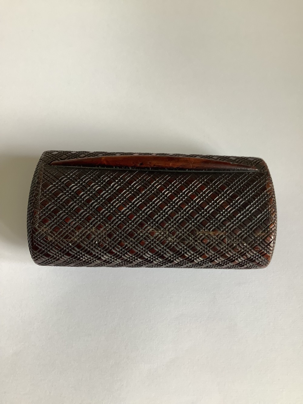 A small hand-carved dark hardwood snuff box featuring a detailed geometric lattice pattern held in a persons hand. View VIII