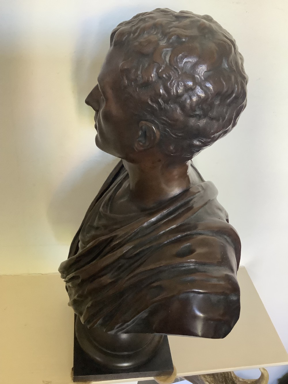 A patinated dark bronze bust depicting a classical Roman emperor with short curled hair and a draped toga, mounted on a turned circular socle and square base. View VI