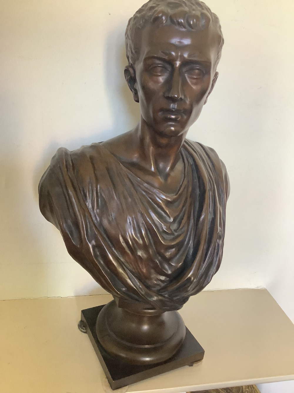 A patinated dark bronze bust depicting a classical Roman emperor with short curled hair and a draped toga, mounted on a turned circular socle and square base. View IX