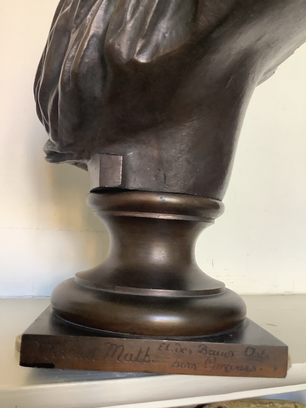 A patinated dark bronze bust depicting a classical Roman emperor with short curled hair and a draped toga, mounted on a turned circular socle and square base. View X