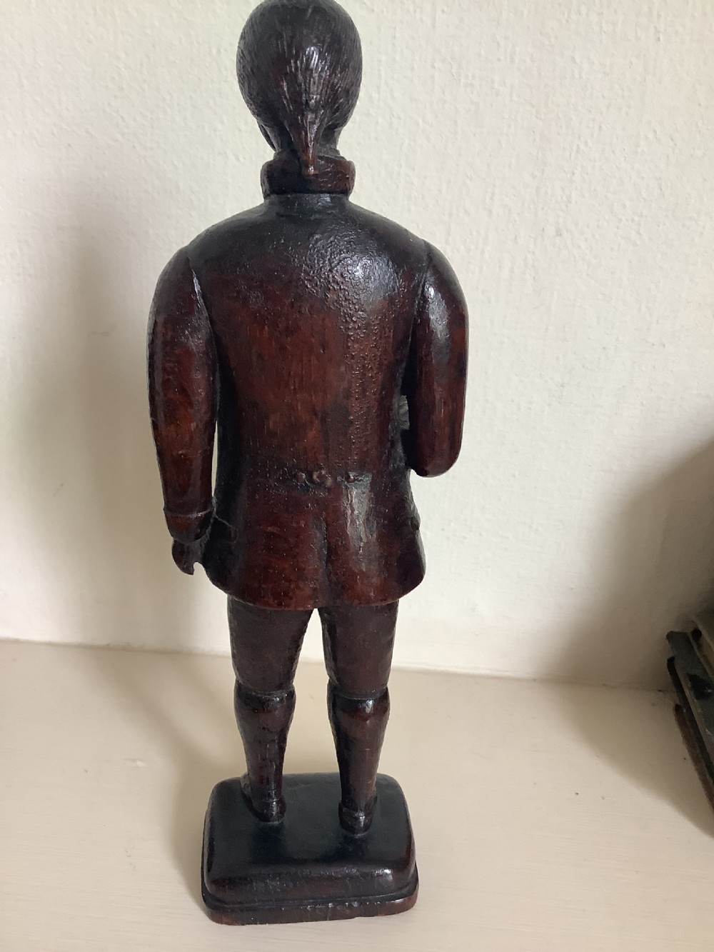 A dark hand-carved wood figure of an 18th-century man holding a book, standing on an integrated wooden base. View V