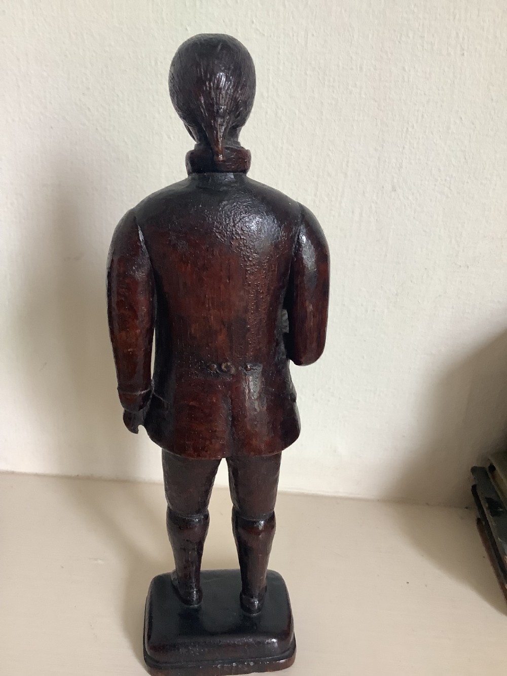 A dark hand-carved wood figure of an 18th-century man holding a book, standing on an integrated wooden base. View IX