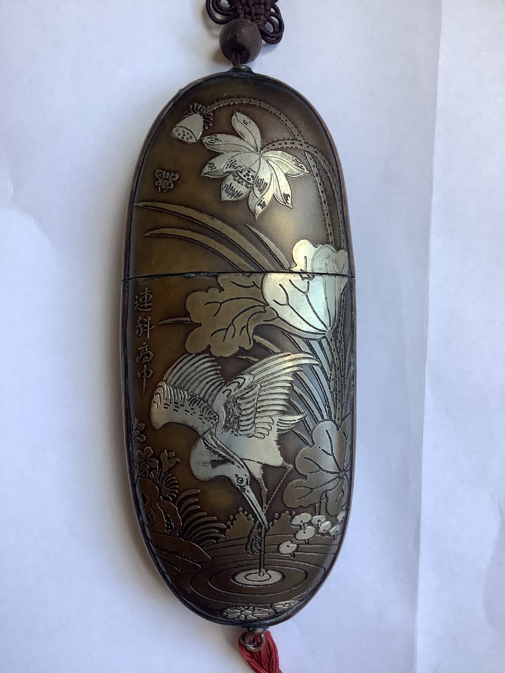 An oval dark bronze Japanese case featuring silver and mixed metal inlaid relief carvings of an elder, child, pine tree, and crane. View III