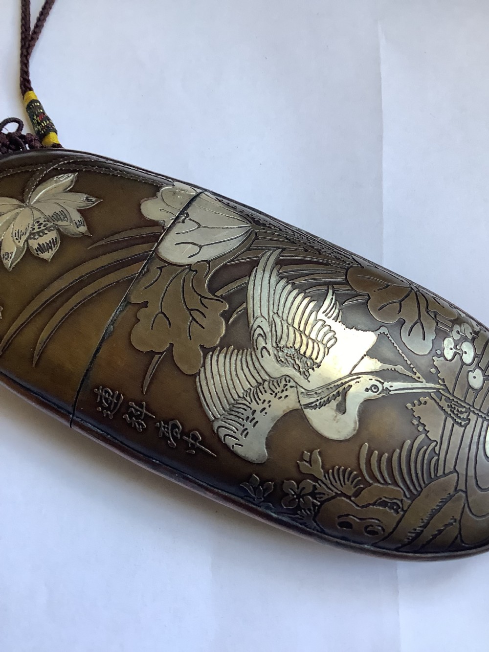 An oval dark bronze Japanese case featuring silver and mixed metal inlaid relief carvings of an elder, child, pine tree, and crane. View VI
