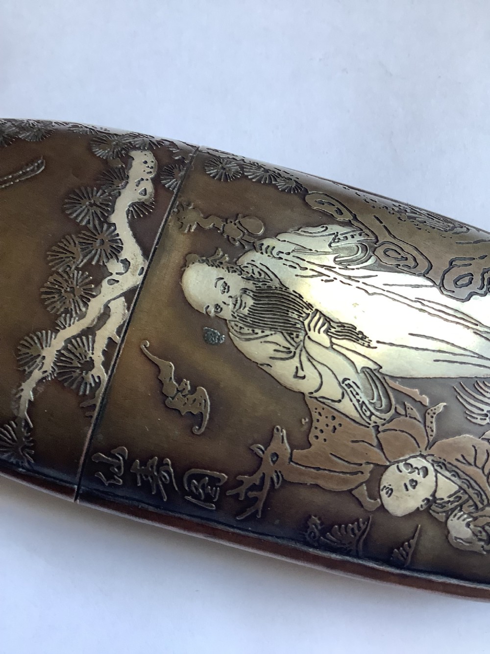An oval dark bronze Japanese case featuring silver and mixed metal inlaid relief carvings of an elder, child, pine tree, and crane. View VII