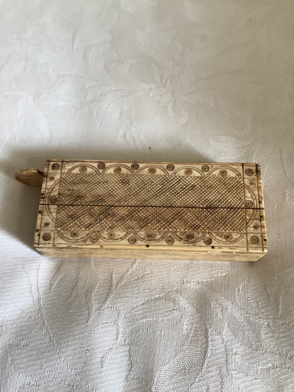 A 19th-century hand-carved bone domino set arranged on a white cloth alongside its decorated sliding wood box, cribbage scoring board, and carved pegs. View VIII
