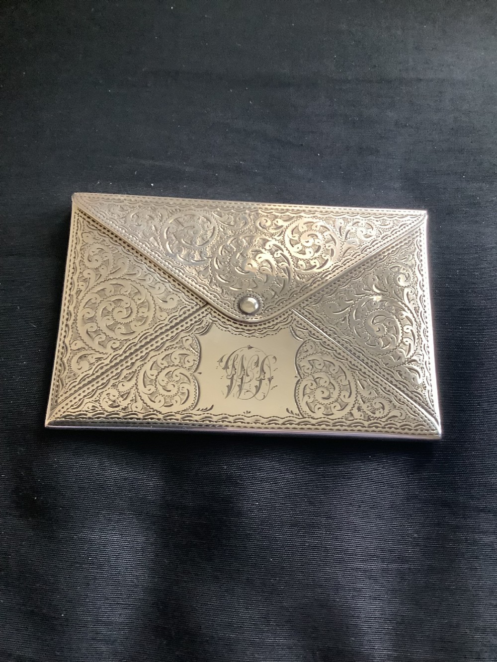 An Edwardian sterling silver card case designed in the shape of an envelope with detailed foliate engraving and a central monogram.