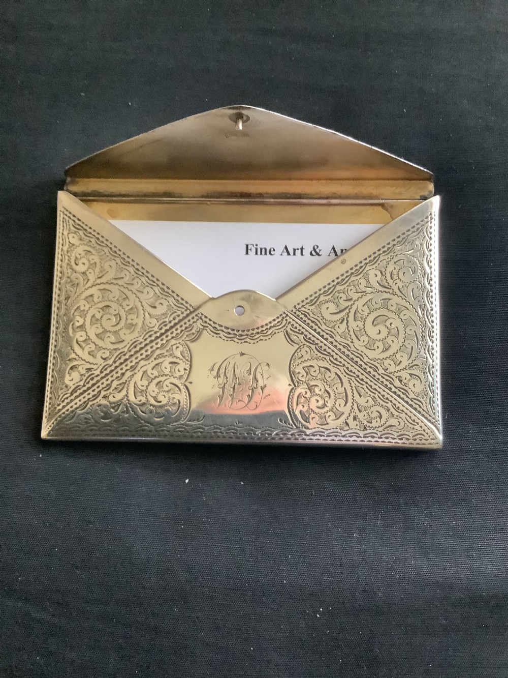 An Edwardian sterling silver card case designed in the shape of an envelope with detailed foliate engraving and a central monogram. View II