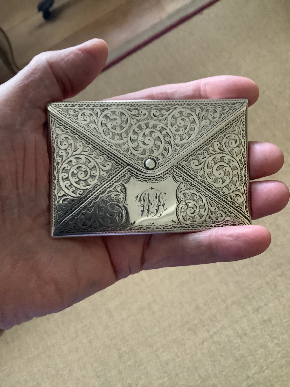 An Edwardian sterling silver card case designed in the shape of an envelope with detailed foliate engraving and a central monogram. View V