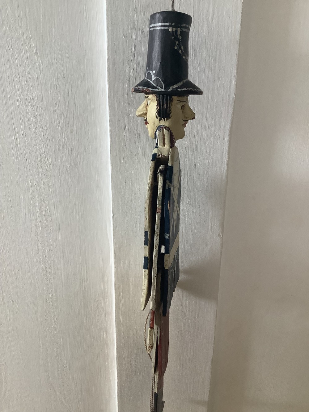 A double-sided flat carved wooden soldier puppet featuring a painted blue jacket, red trousers, black boots, tall black shako hat, and central hanging string. View VIII