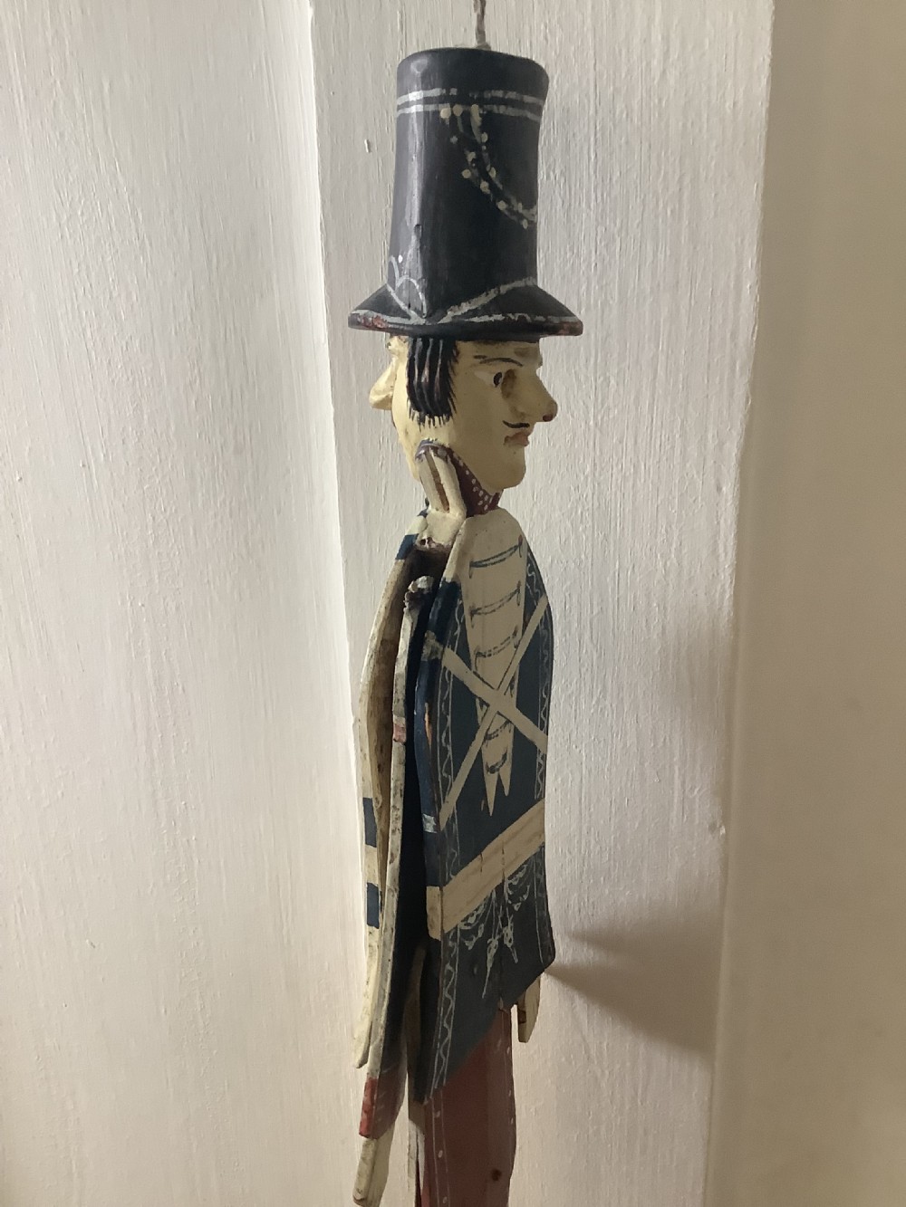 A double-sided flat carved wooden soldier puppet featuring a painted blue jacket, red trousers, black boots, tall black shako hat, and central hanging string. View IX
