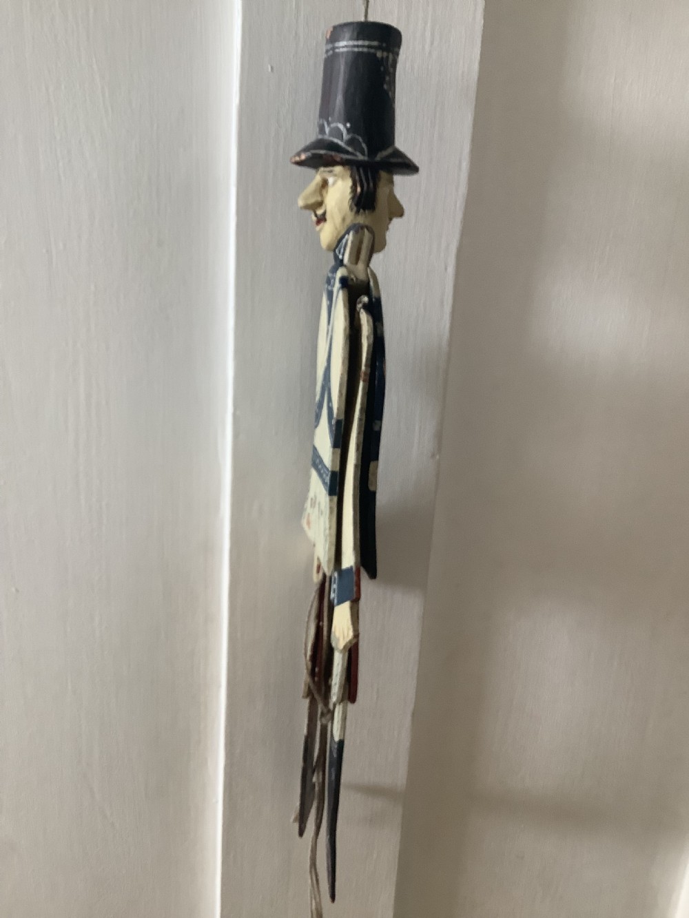 A double-sided flat carved wooden soldier puppet featuring a painted blue jacket, red trousers, black boots, tall black shako hat, and central hanging string. View XII