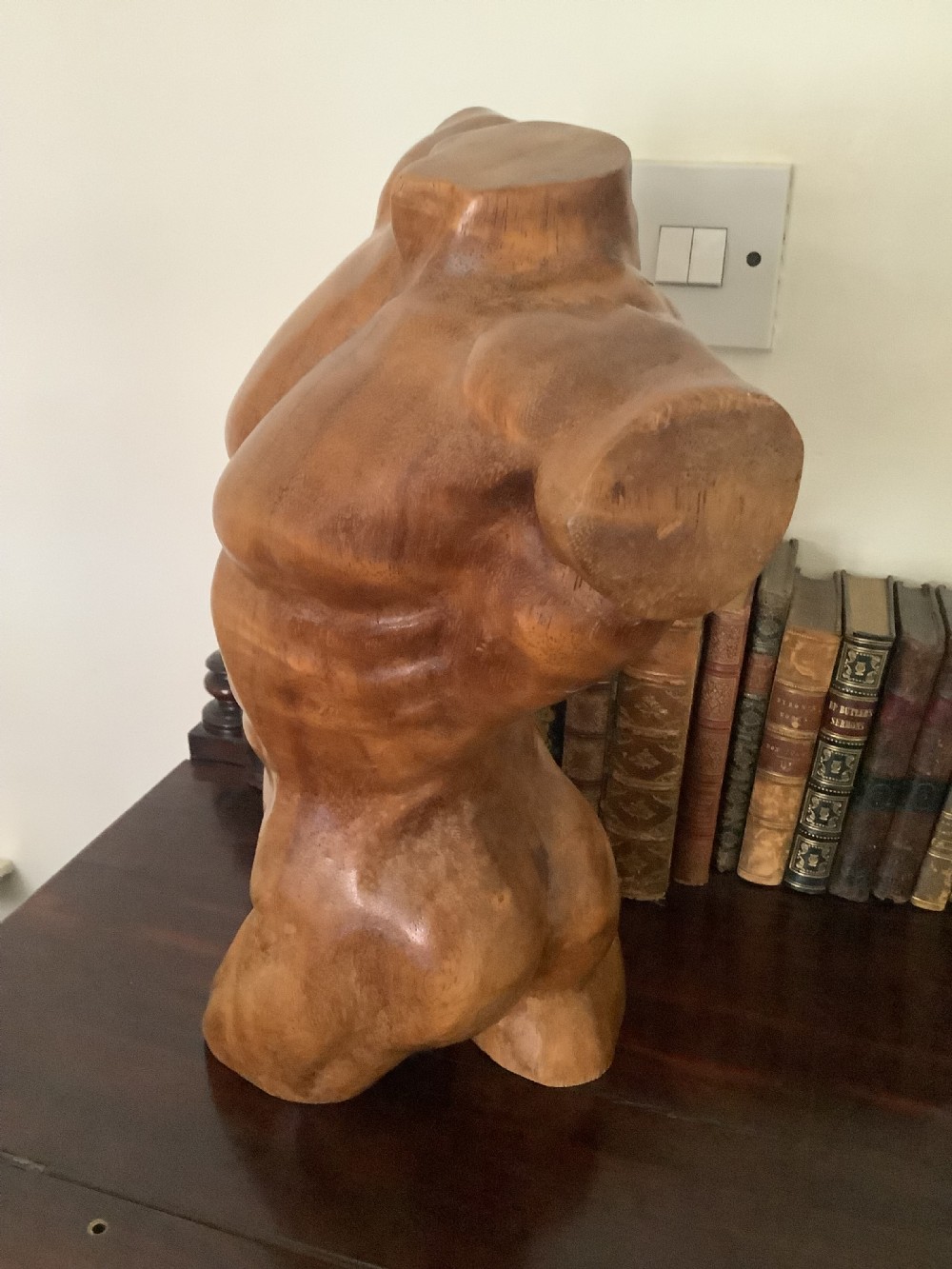 A three-dimensional carved hardwood sculpture depicting a classical male torso with defined muscle structure and a smooth polished finish.