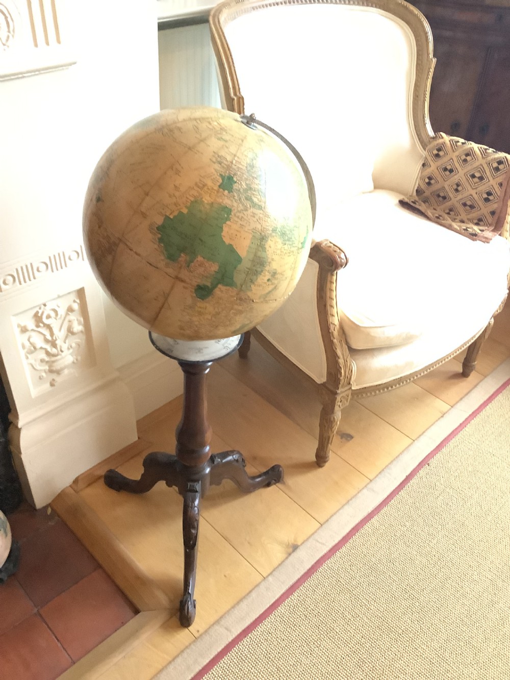 A terrestrial floor-standing globe mounted on a brass half-meridian, supported by a turned mahogany column with carved tripod cabriole legs.