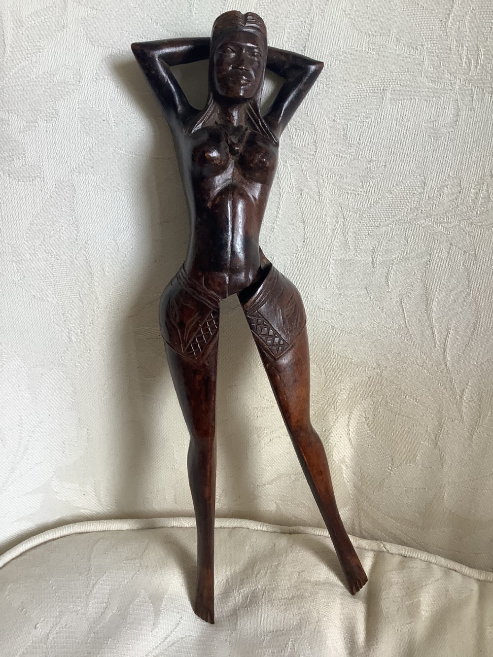 A hand-carved dark wood nutcracker sculpted in the form of a standing woman with her arms raised behind her head.