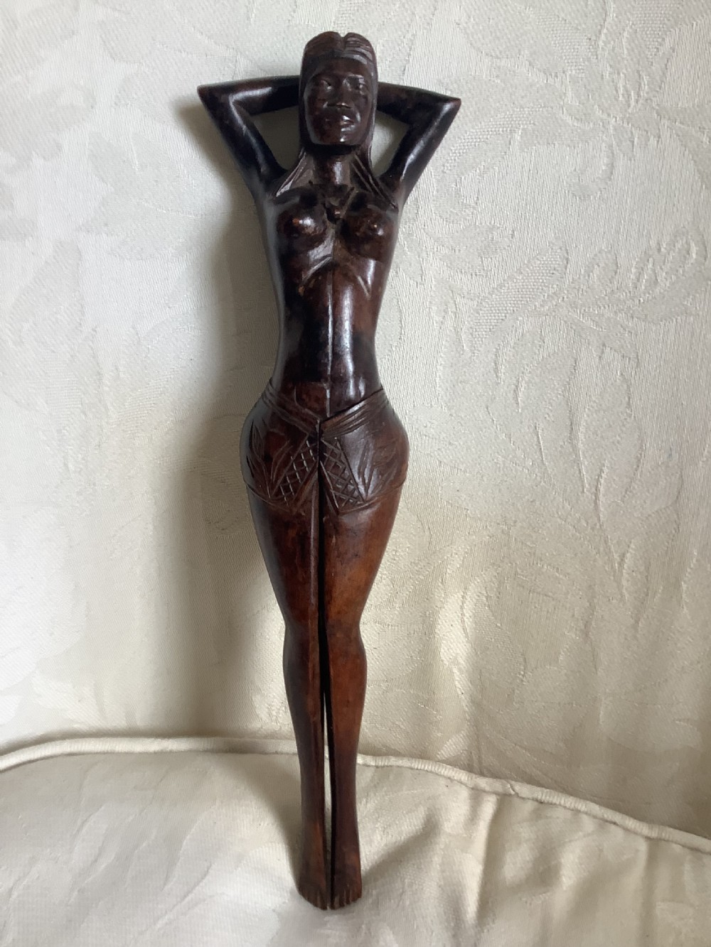 A hand-carved dark wood nutcracker sculpted in the form of a standing woman with her arms raised behind her head. View II