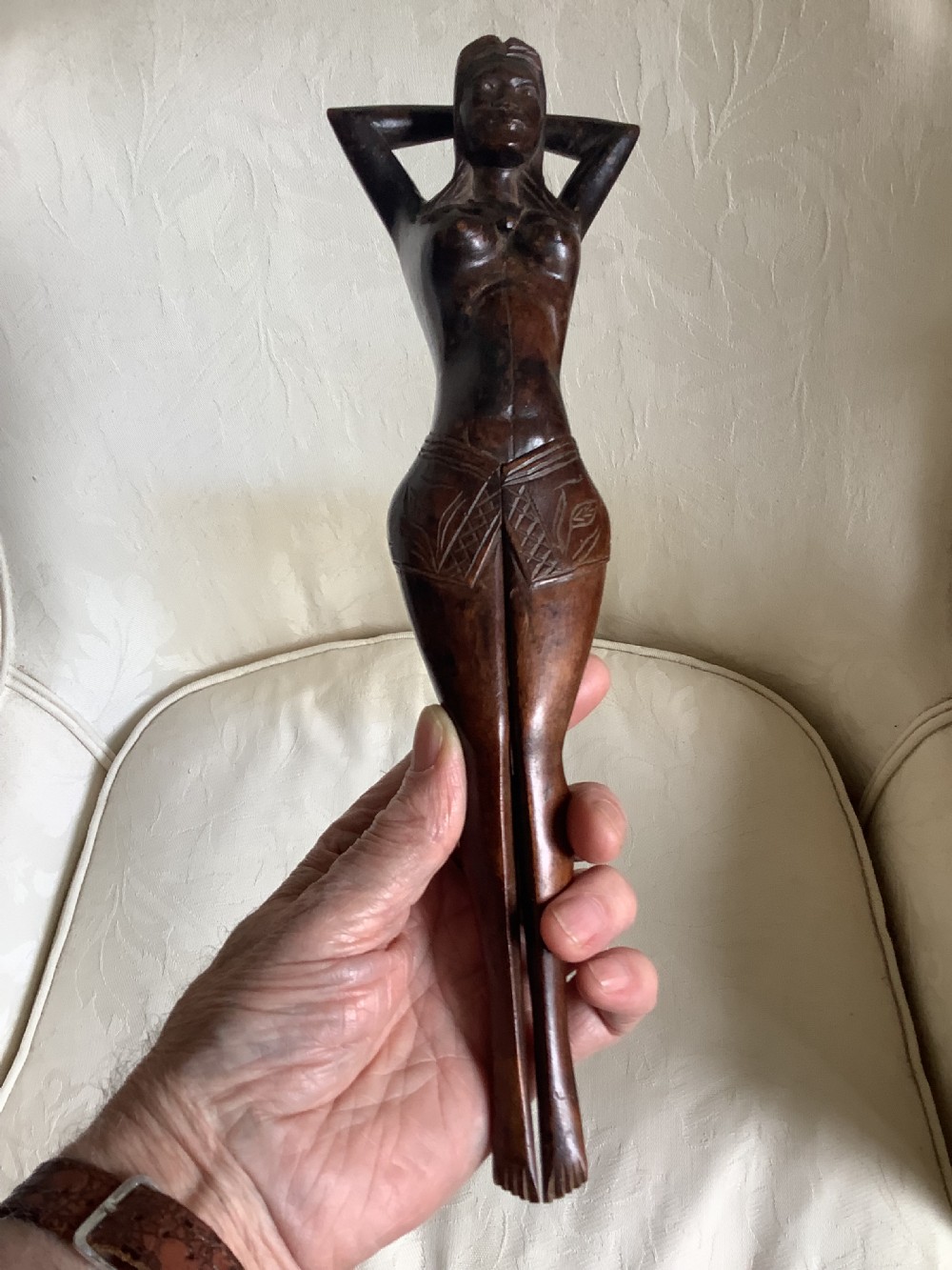 A hand-carved dark wood nutcracker sculpted in the form of a standing woman with her arms raised behind her head. View III