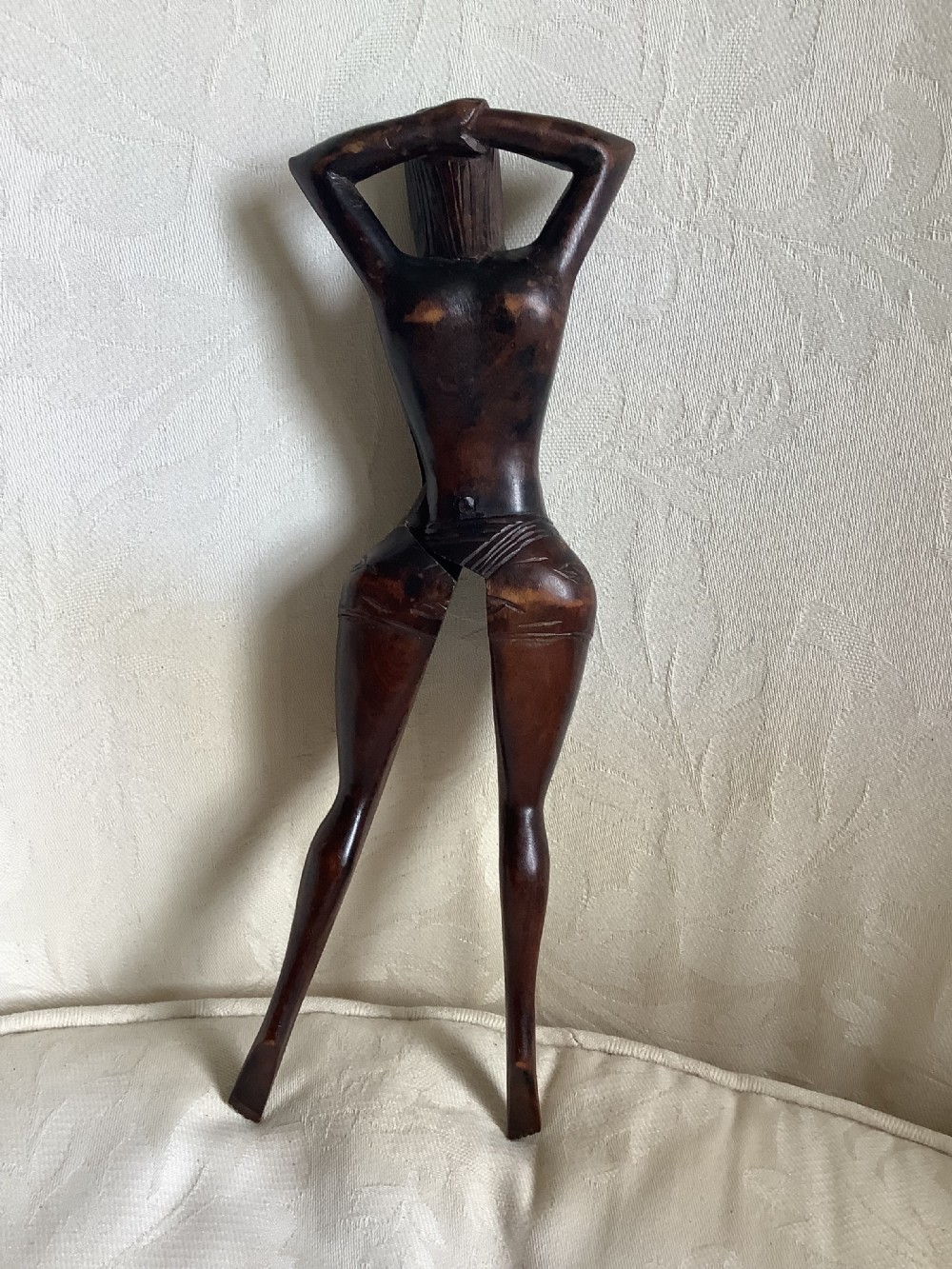 A hand-carved dark wood nutcracker sculpted in the form of a standing woman with her arms raised behind her head. View IV